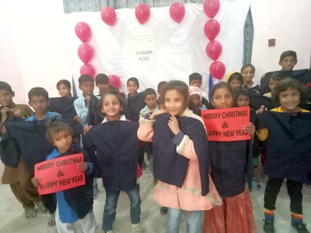 Schülerinnen und Schüler der St. Peter's School halten Schilder mit "Merry Christmas & Happy New Year" und warme Pullover hoch, die sie geschenkt bekommen haben